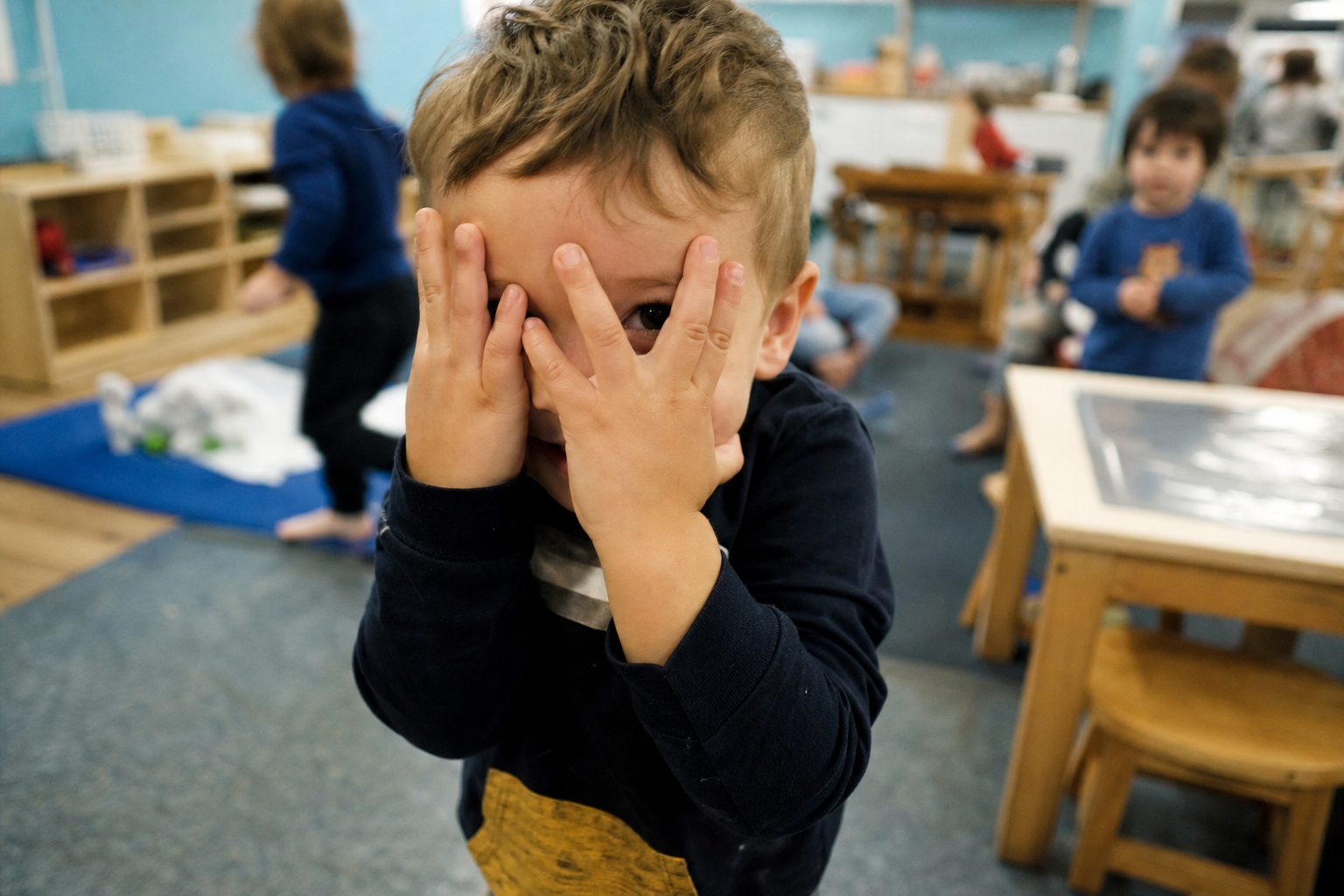 Child with their hands over their face peeking through fingers