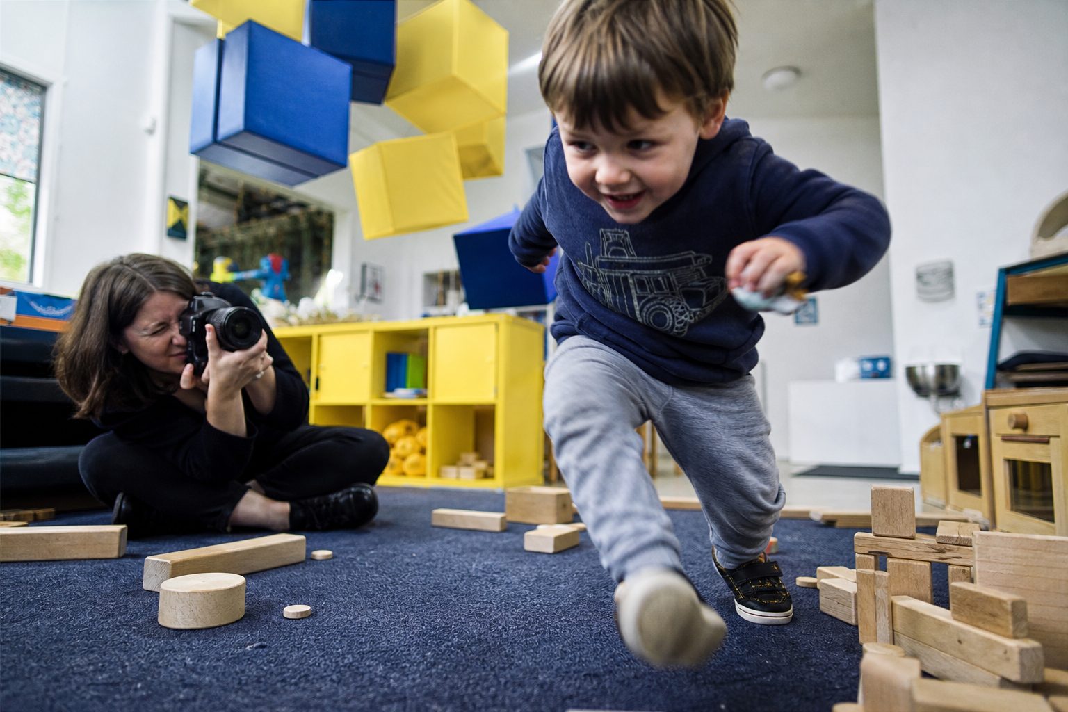 Photographer crouched low on the floor of a childcare room with a camera