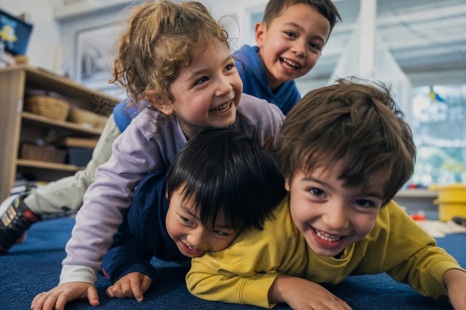 Group of four kids piled on top of each other laughing