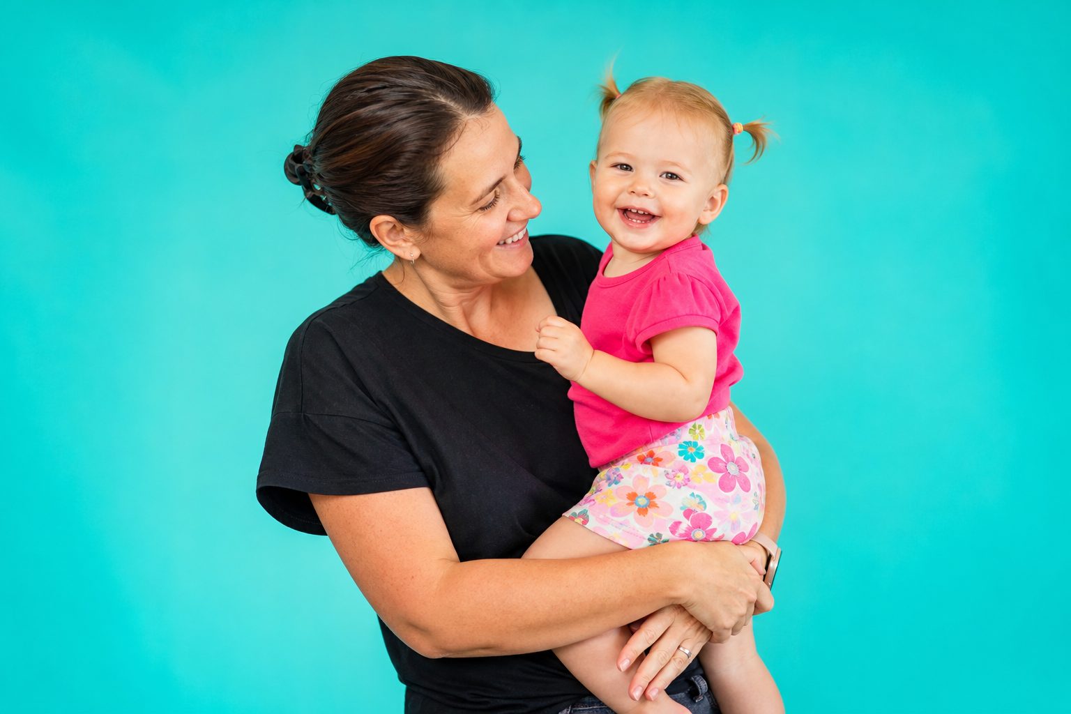 Educator holding a smiling baby against a bright coral backdrop