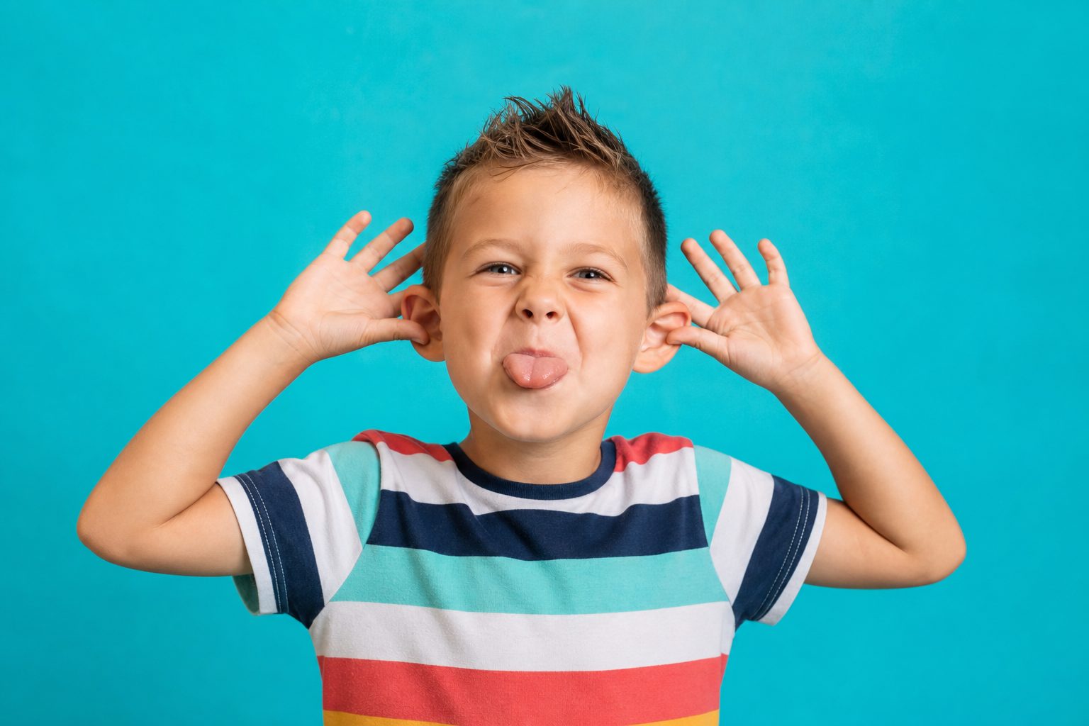 Child against a turquoise backdrop pulling a silly face