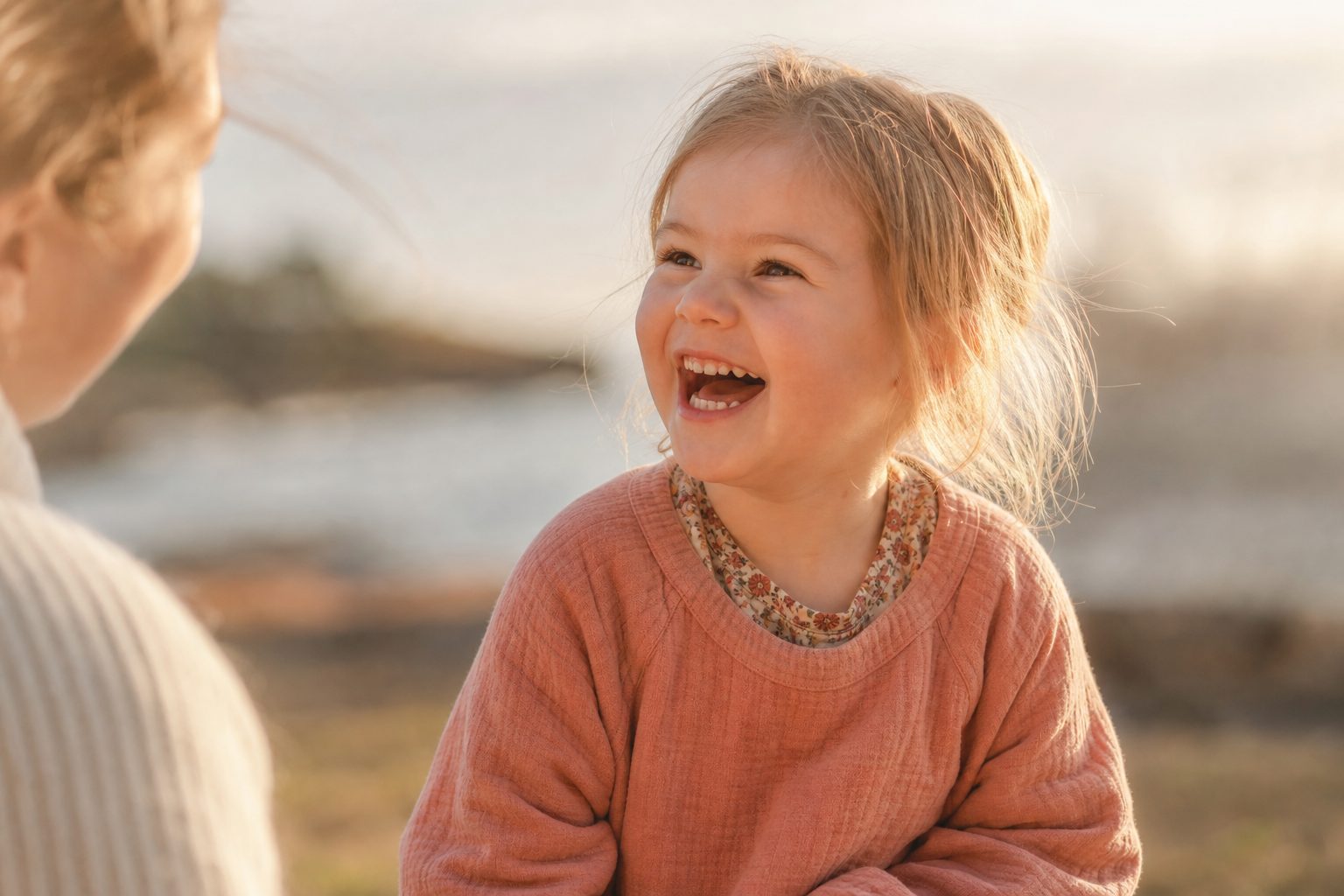Child laughing in warm sunlight against a soft coastal background