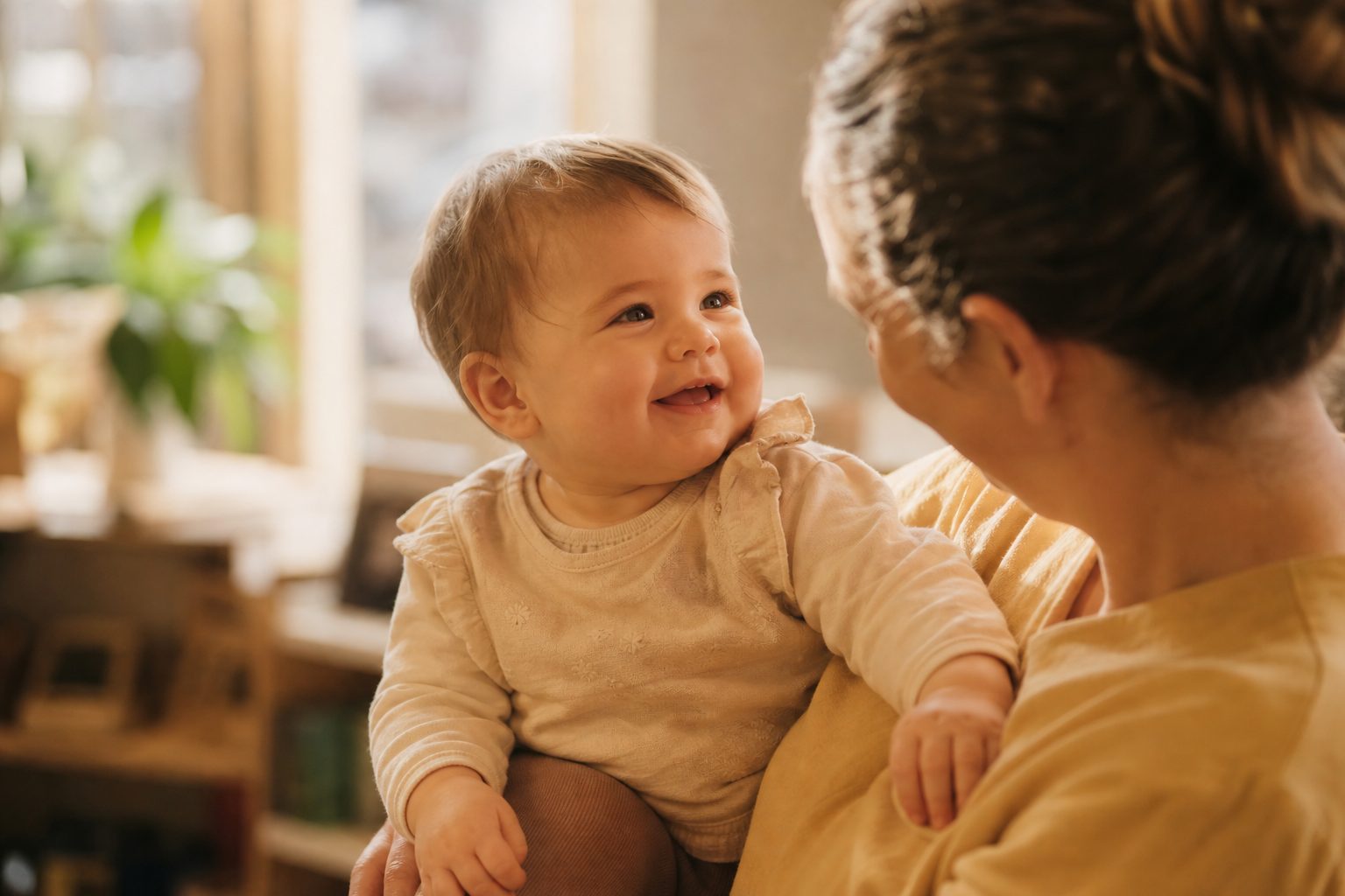 Baby smiling in soft warm light held by an educator